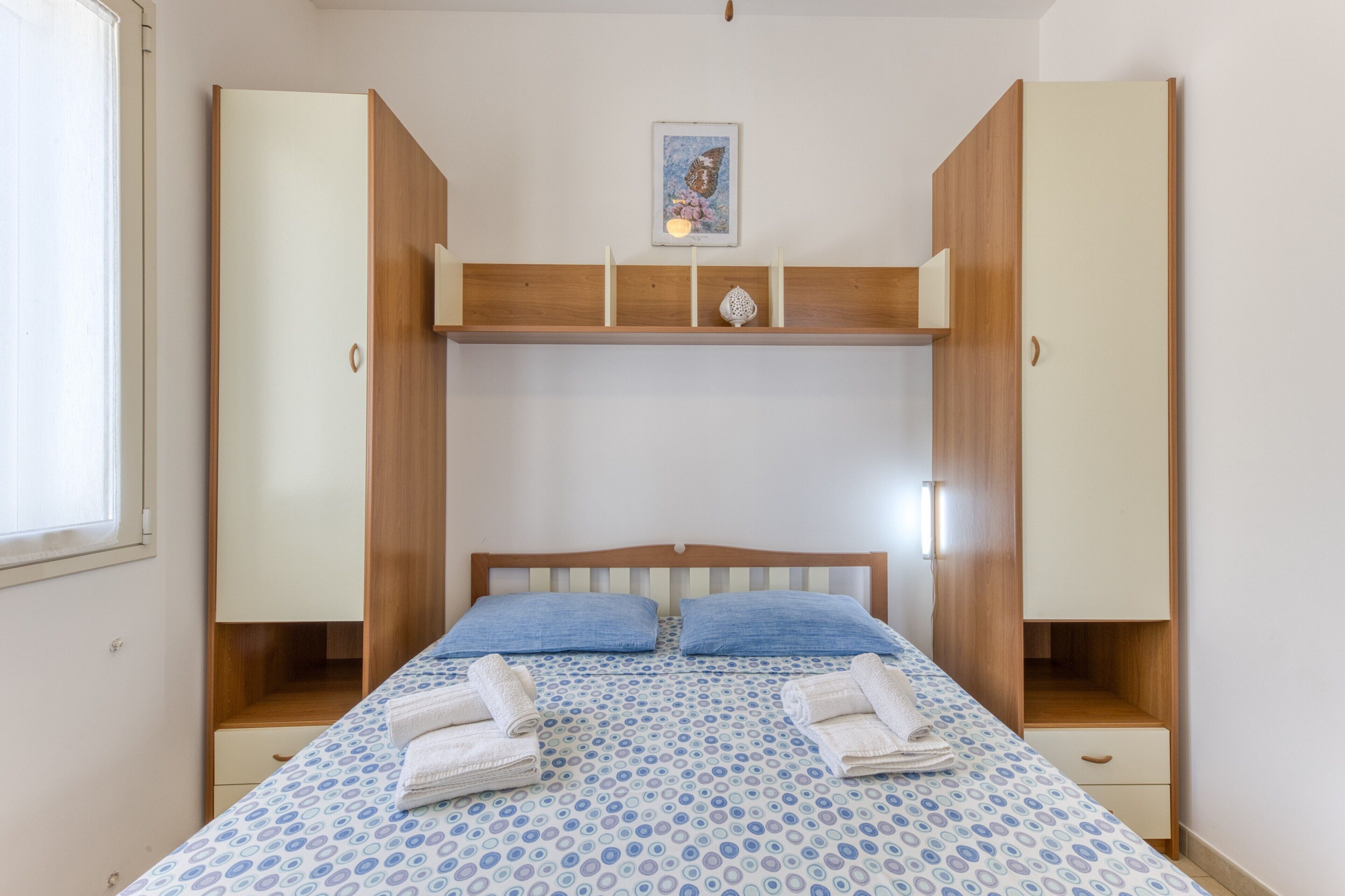 Ein Schlafzimmer mit einem Bett, einem Holzschrank und einem Regal mit einem Bild.