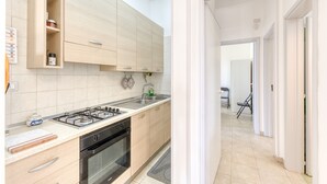 A modern kitchen with a gas stove, oven, and a sink. There is a wooden cabinet with a shelf above the sink.