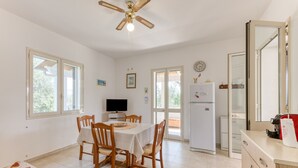 A kitchen with a dining table, chairs, a ceiling fan, a refrigerator, and a television.