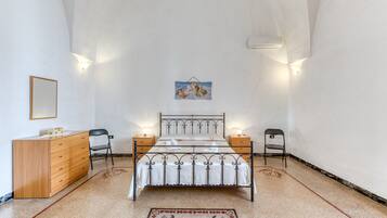 A bedroom with a bed, dresser, two chairs, bedside tables, and a wall-mounted air conditioner.