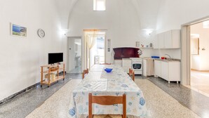 Un grand espace dédié à la salle à manger, avec une longue table, des chaises, un téléviseur et un coin cuisine équipé de placards et d’un évier.