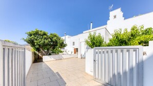 Une cour avec un portail blanc, un arbre et un bâtiment à la façade blanche.