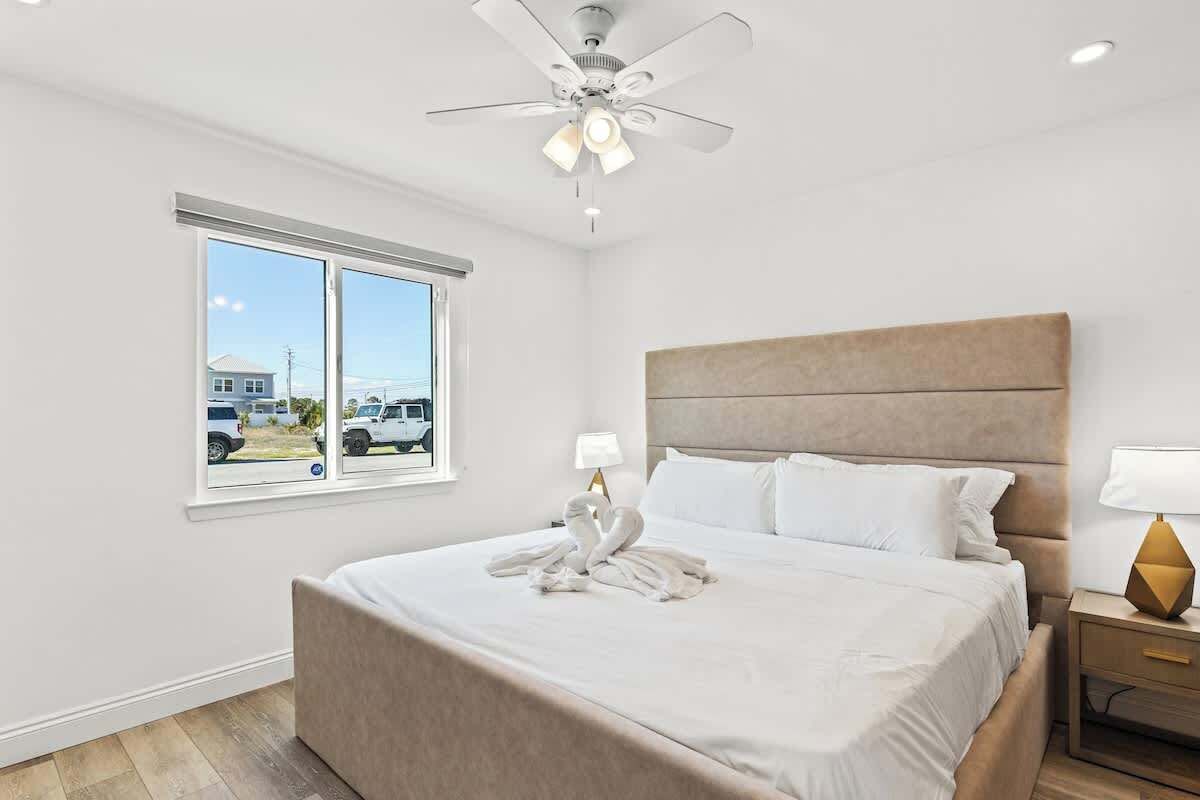 Una habitación de hotel con una cama grande, un ventilador de techo, un ventanal con vistas al exterior y una mesita de noche con lámpara.