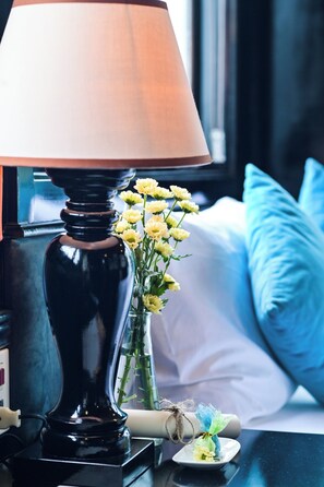 Une lampe de table noire avec un abat-jour blanc, un vase rempli de fleurs jaunes et un coussin bleu sur un lit.