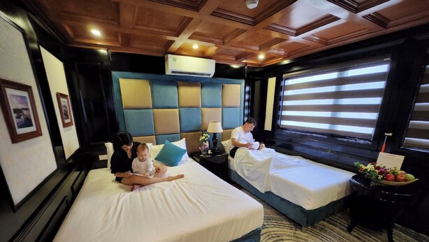 Une chambre d’hôtel avec deux lits, une grande fenêtre avec stores, un ventilateur de plafond et un climatiseur fixé au mur.