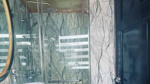 Une salle de bain avec un meuble-lavabo en bois, un grand miroir, un lavabo blanc, un meuble noir et une cabine de douche en verre.
