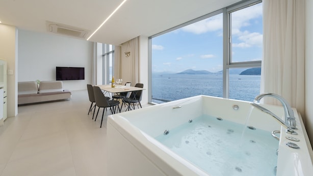 A modern hotel room with a large bathtub, a dining area, and a sofa. - Geoje Lighthouse Pension (Geoje)