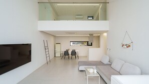 A modern living room with a sofa, a TV, and a dining area with chairs and a table. - Geoje Lighthouse Pension (Geoje)