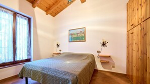 A bedroom with a bed, wooden wardrobe, a painting on the wall, and a window with curtains.