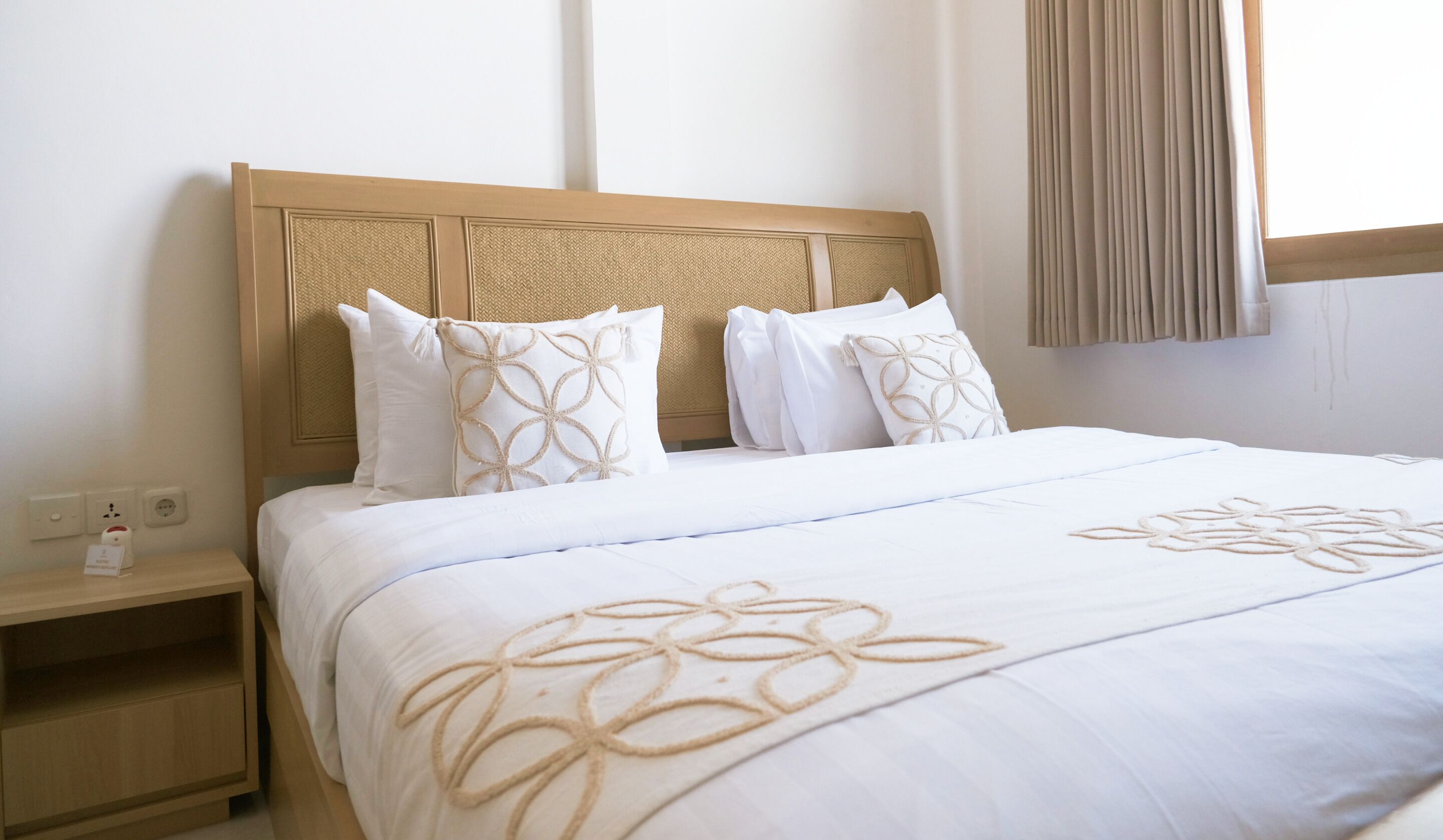 A hotel room with a wooden headboard, white bedding, and a nightstand with a lamp.