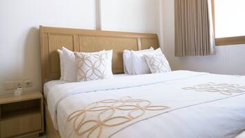 A hotel room with a wooden headboard, white bedding, and a nightstand with a lamp.