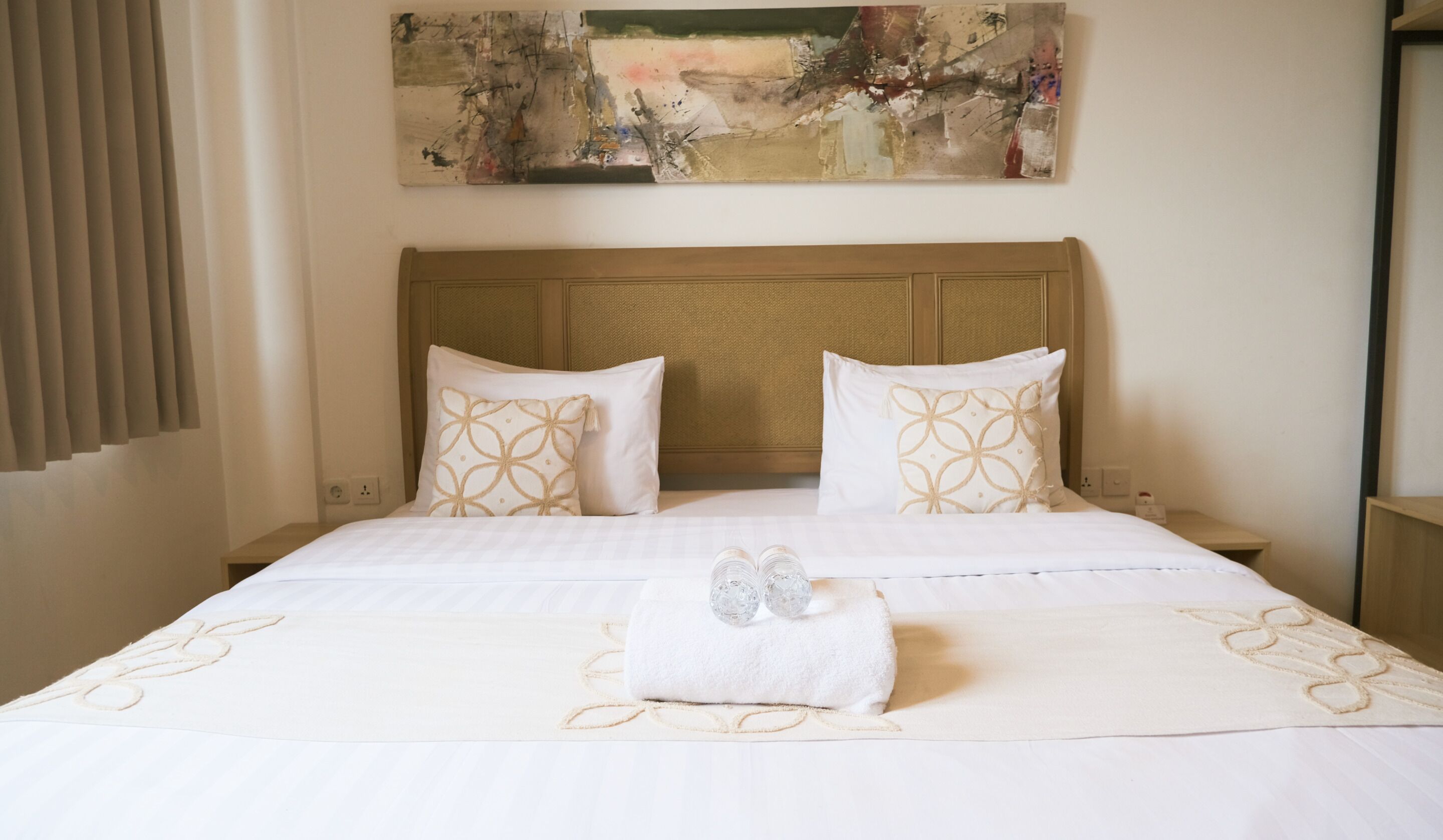 Une chambre d’hôtel avec un grand lit, deux oreillers à motifs géométriques, une serviette sur le lit et un tableau au-dessus du lit.