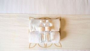 Una cama ordenada con un almohadón y dos botellas de agua encima.