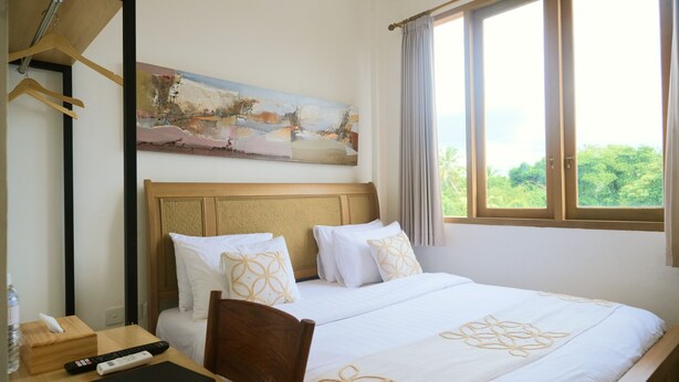Una habitación de hotel con cama, un cuadro en la pared, una ventana con cortinas y un escritorio con control remoto.