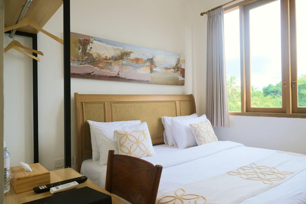 Een hotelkamer met een bed, een schilderij aan de muur, een raam met gordijnen en een bureau met een afstandsbediening.