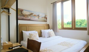 Una habitación de hotel con cama, un cuadro en la pared, una ventana con cortinas y un escritorio con control remoto.