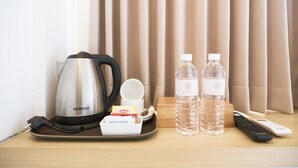 Una bandeja con una tetera, dos botellas de agua, una caja de té Lipton, un control remoto y un adaptador de corriente sobre una superficie de madera.