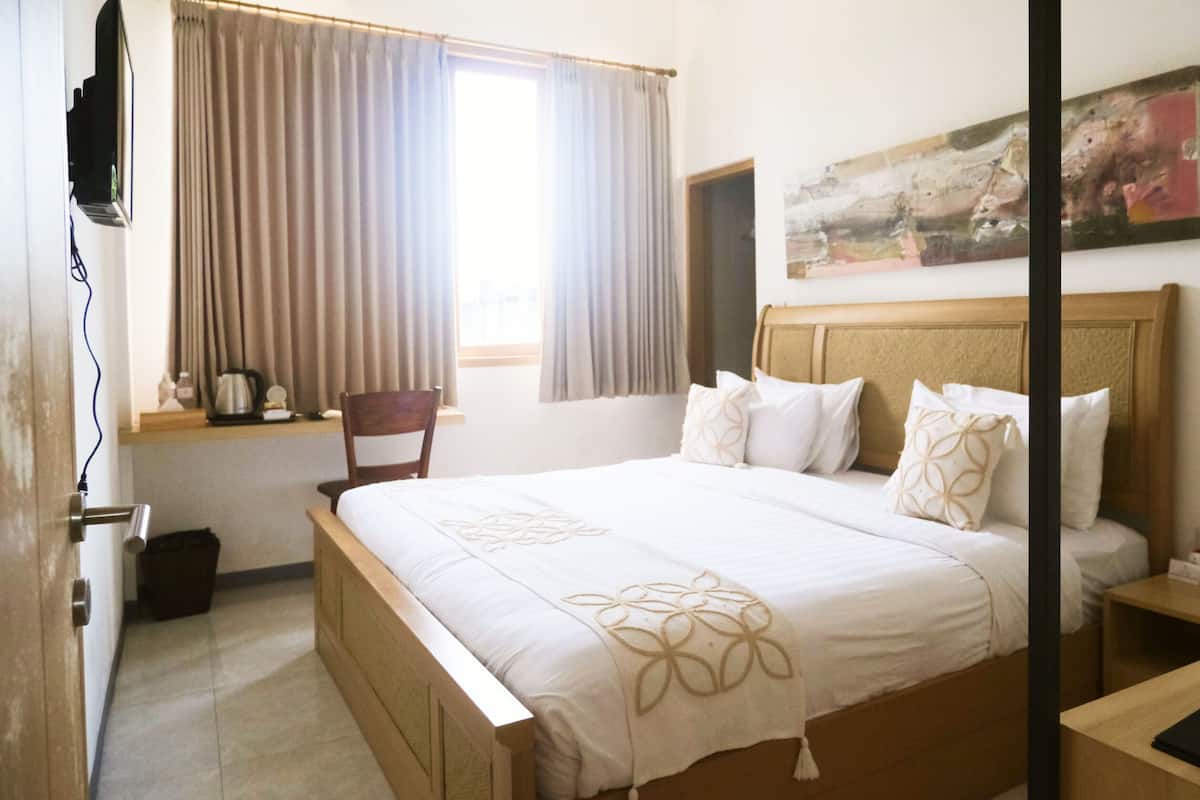 Een hotelkamer met een bed, nachtkastje, stoel, raam met gordijnen, schilderij aan de muur en een aan de wand bevestigde televisie.
