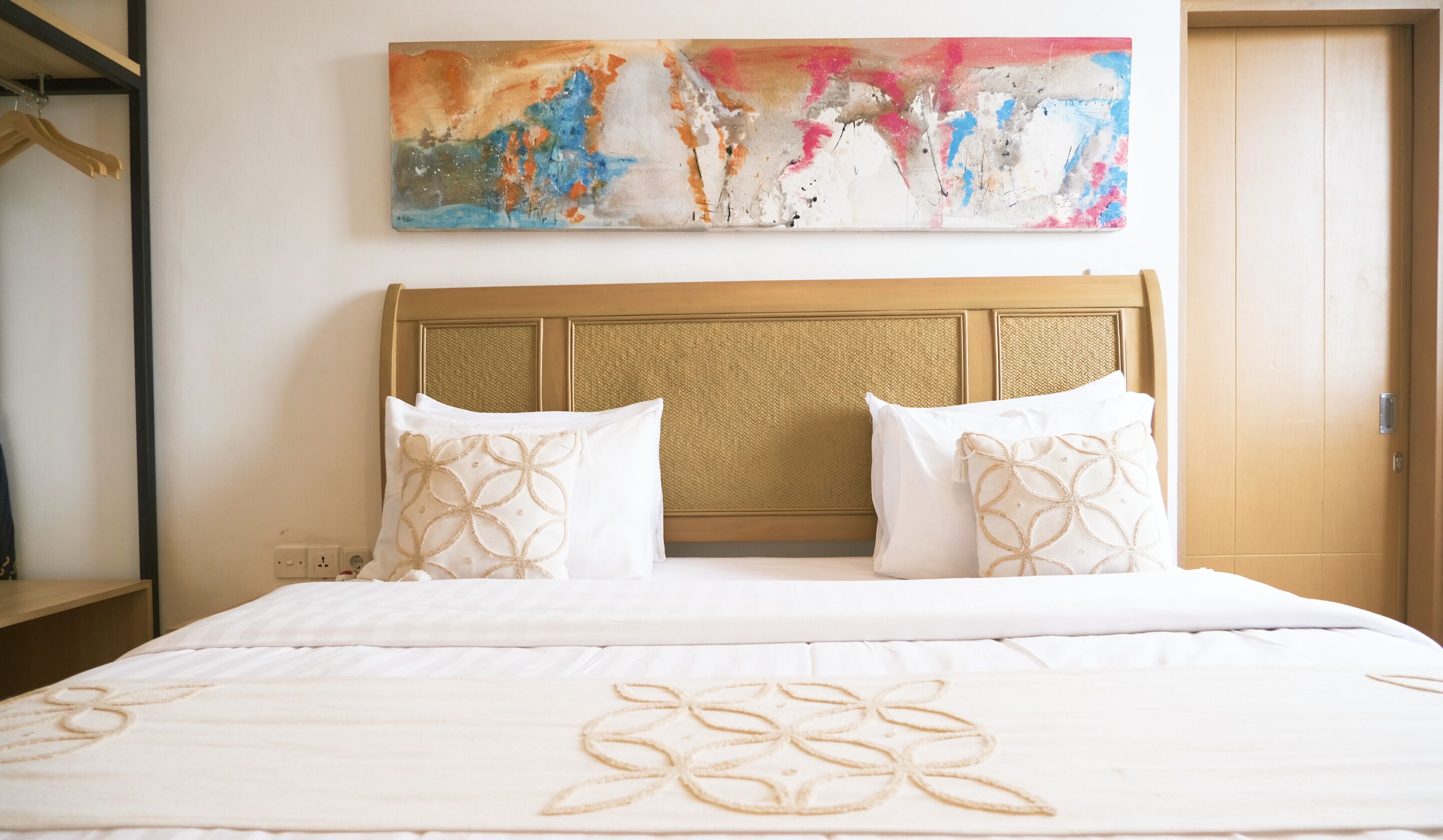 Habitación de hotel con cama, dos almohadas, cabecero y un cuadro abstracto colorido en la pared.