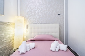 A hotel room with a bed, a wall-mounted light, a textured wall, and a tiled floor.