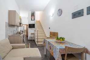 A compact living space with a kitchenette, a dining area with a patterned tablecloth, a sofa, and a staircase leading to an upper level.