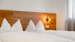 Une chambre d’hôtel avec une tête de lit en bois, du linge de lit blanc et un luminaire fixé au mur.