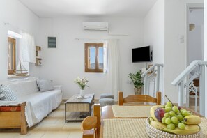 A modern, well-lit living room with a sofa, a dining table with fruit, a TV, and a staircase.