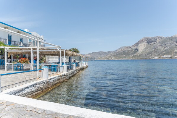 A waterfront building with a balcony, a pier extending into the water, and a mountainous backdrop.