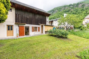 Un bâtiment à deux étages doté d’une façade en bois, d’un petit jardin et surplombant un paysage montagneux.