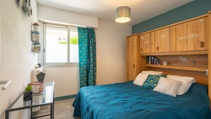 Une chambre à coucher comprenant un lit, une table de chevet, une fenêtre avec des rideaux, une armoire en bois et un luminaire au plafond.