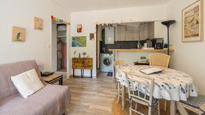 Un espace de vie compact comprenant un canapé, une table à manger et un coin cuisine équipé d’un lave-linge.