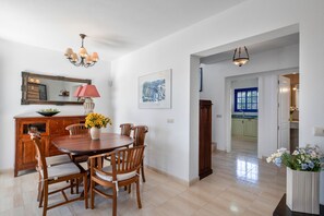 A dining area with a wooden table and chairs, a vase with flowers, a mirror, and a chandelier.