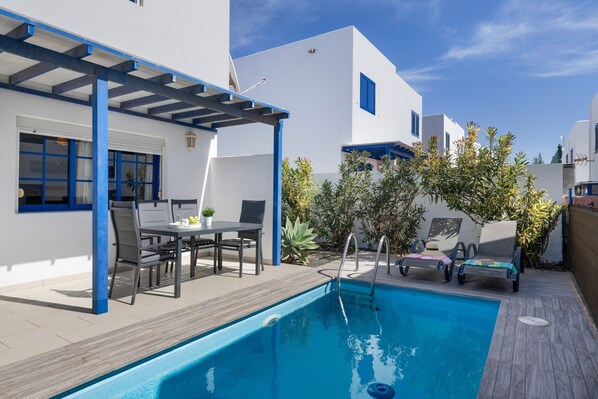 A poolside area with a table and chairs, a pergola, and a pool.