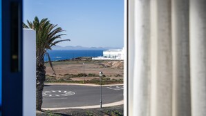 A view of a coastal road with a palm tree, a white building, and the ocean in the background.