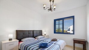 A bedroom with a bed, bedside tables, a nightstand, a wooden nightstand, a window with a view, and a chandelier.