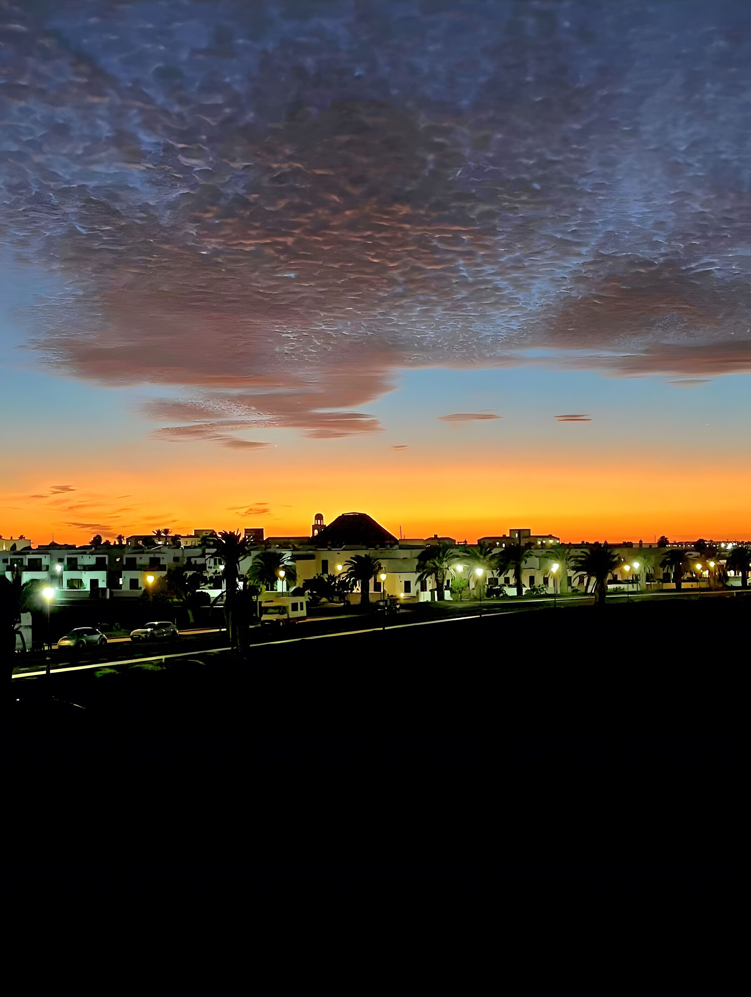 A sunset over a cityscape with buildings and palm trees.