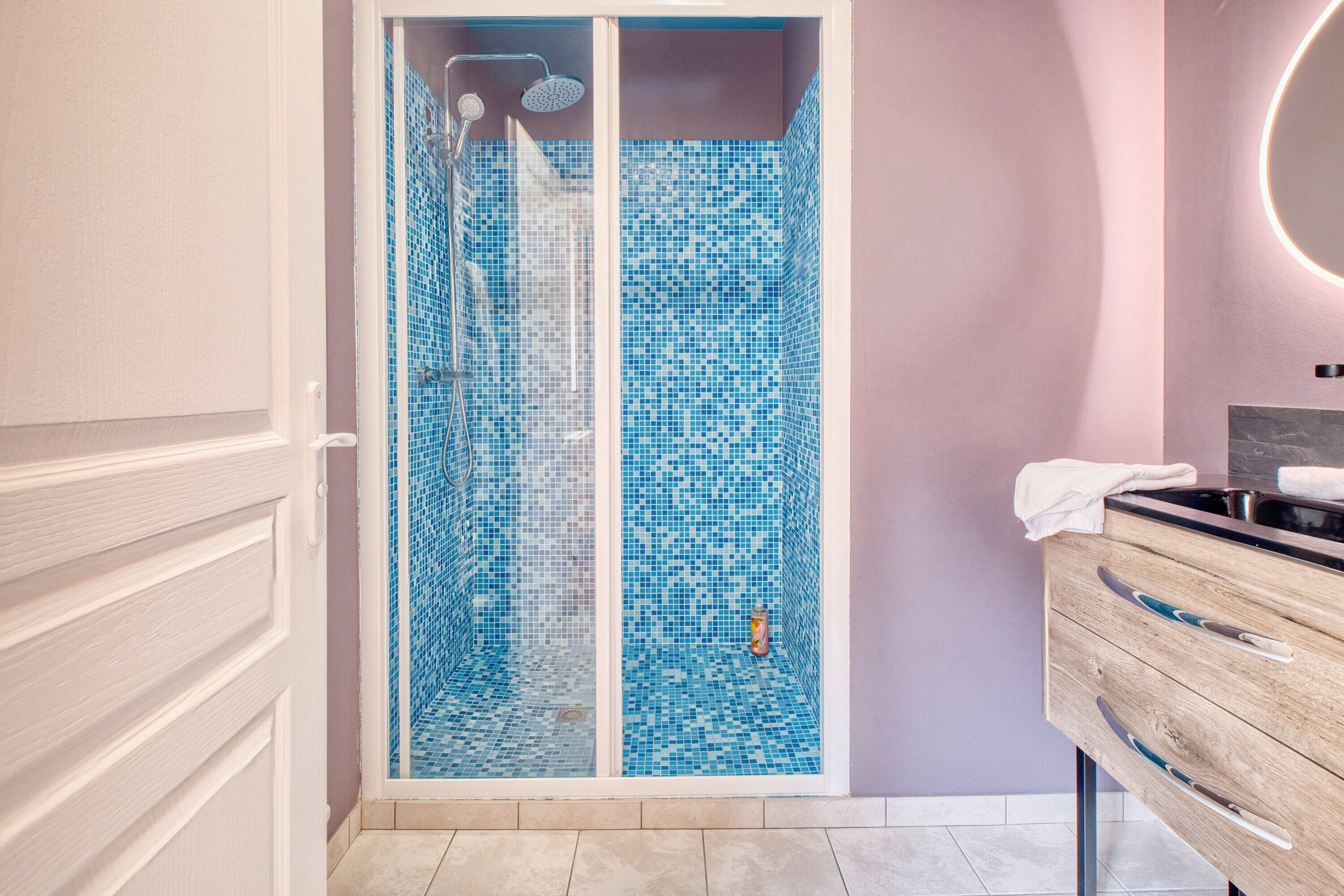 A bathroom with a shower, a vanity with a mirror, and a tiled floor.