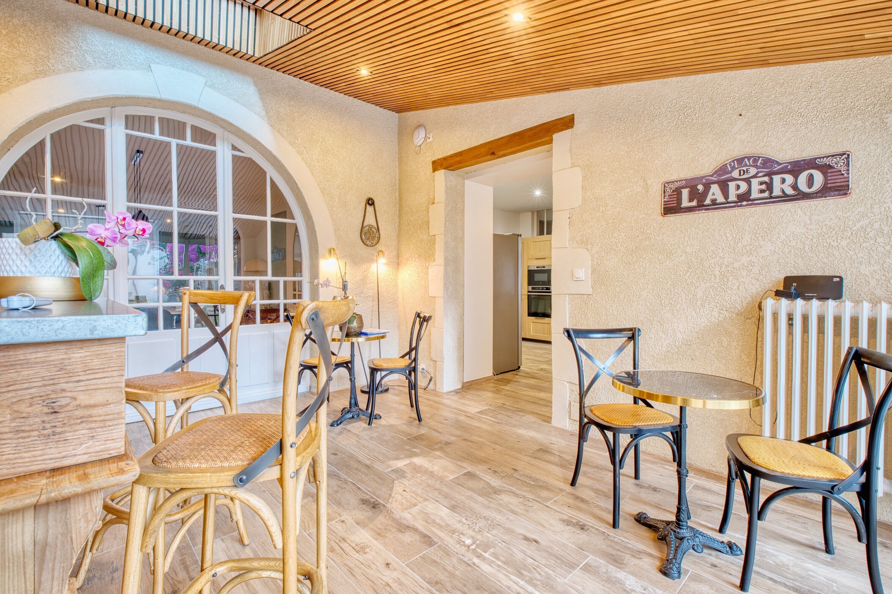 A dining area with wicker chairs, a wooden table, and a sign reading 'Place de L'Apero.'