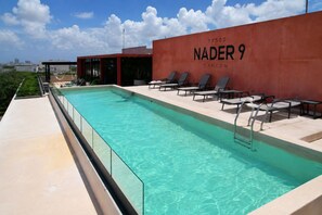 A swimming pool with lounge chairs and a red wall with the text 'NADER 9 Cancun'. - Condo in Cancun with Pool, Gym and Coworking | Pet friendly, near ZH (Cancún)