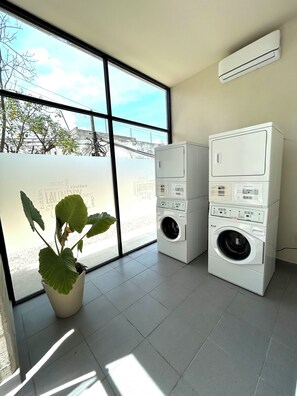 A laundry room with stacked washers and dryers, a large potted plant, and a view through a large window. - Condo in Cancun with Pool, Gym and Coworking | Pet friendly, near ZH (Cancún)