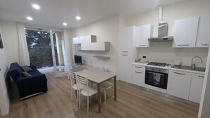 A modern kitchen with white cabinets, a dining table with chairs, a built-in stove, and a large window with a view of trees.