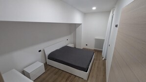 A bedroom with a single bed, a nightstand, a radiator, and a white wall.