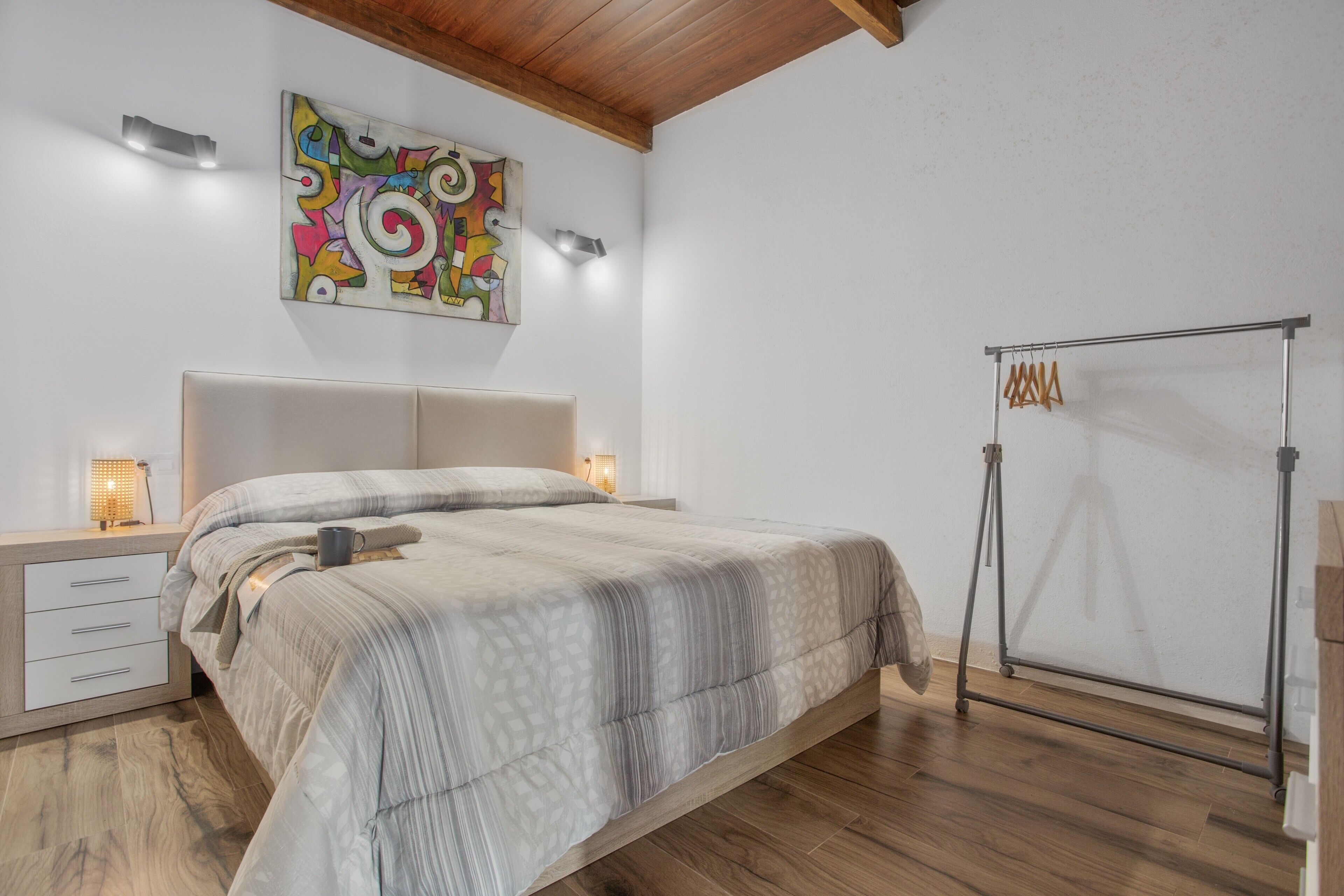 A bedroom with a bed, bedside tables, a wall-mounted artwork, and a tripod stand.