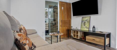 Una sala moderna con un sofá, una mesa de centro, un televisor montado en la pared y una puerta de madera.