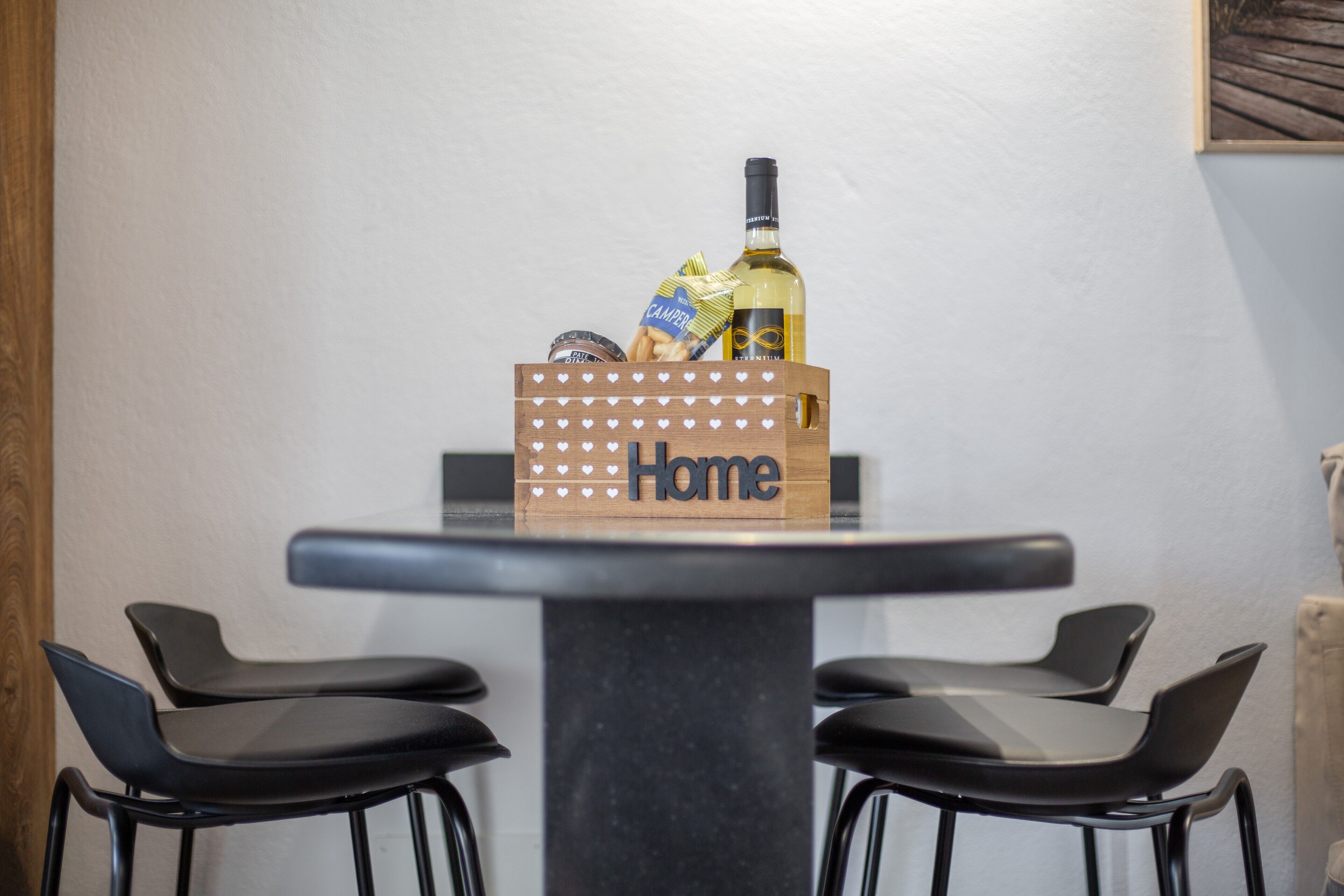 Taula amb una caixa de fusta que diu 'Home', amb una ampolla i alguns aliments a dins.