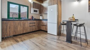 A kitchen with wooden cabinets, a microwave, a refrigerator, a bar stool, and a table.
