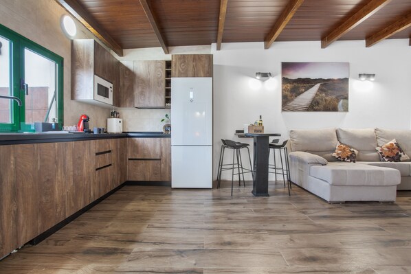A modern kitchen with wooden cabinets, a white refrigerator, and a dining area with a sofa and chairs.