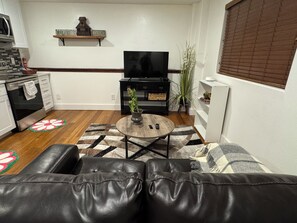 Una sala de estar con un sofá de cuero, una mesa de centro, un televisor y una cocina al fondo.