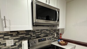 Une cuisine moderne avec des armoires blanches, un four à micro-ondes en acier inoxydable, un four encastré et un pare-feu décoratif.