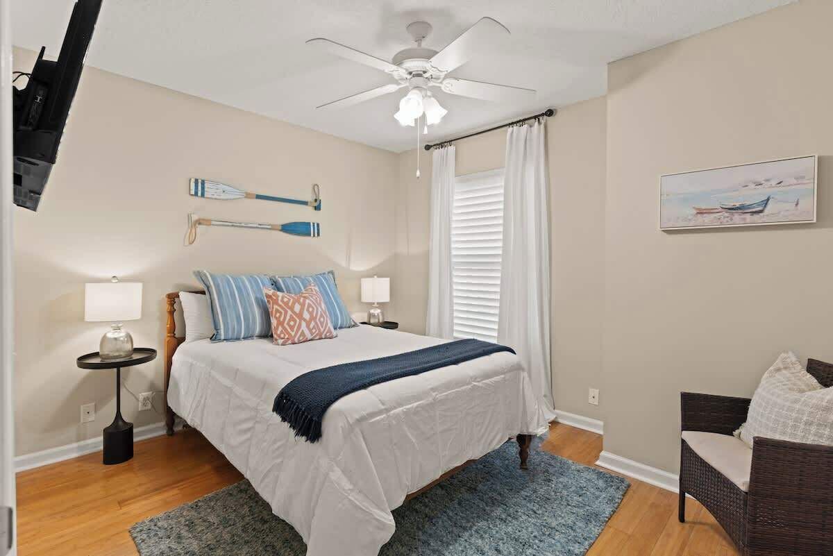 A bedroom with a bed, a ceiling fan, a painting, and a window with curtains.